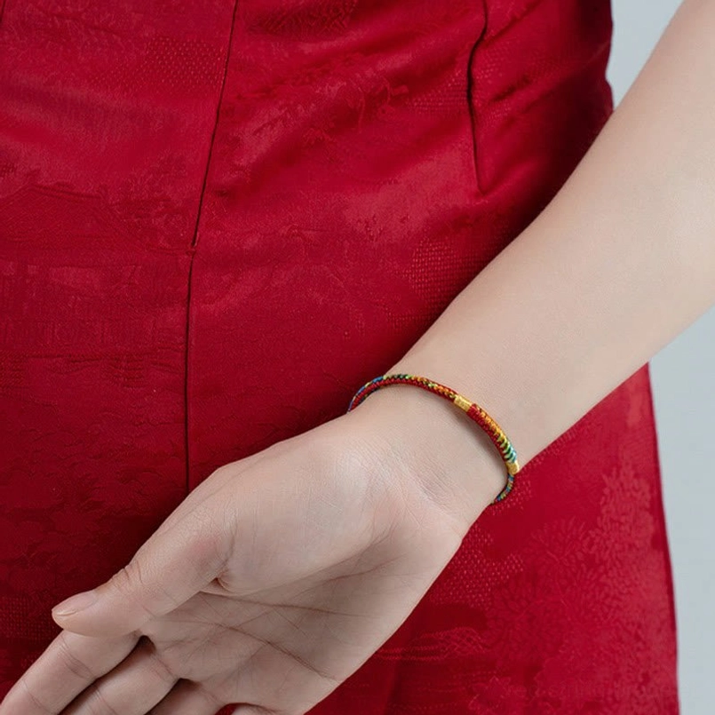 Red string bracelet stacked with other dainty spiritual jewelry on neutral background
