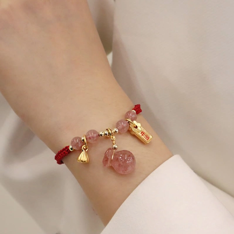Strawberry quartz red string bracelet worn on wrist showing side view with lotus drop charm and fortune tag pendant against light colored clothing