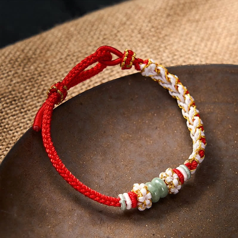 Chinese knot red cord bracelet with jade beads styled on burlap and ceramic tray