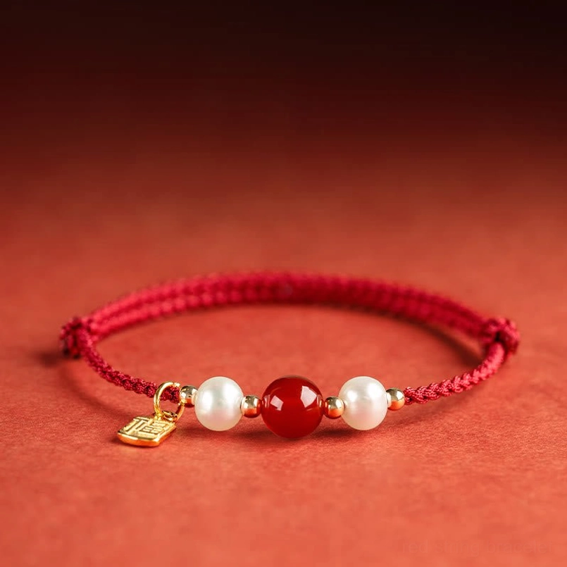 Symmetrical red string fortune bracelet with central red agate, white pearls and square gold charm overhead view