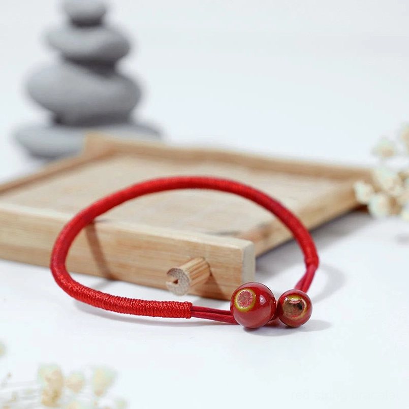Three-quarter side view of adjustable red string bracelet with ceramic beads and wooden background