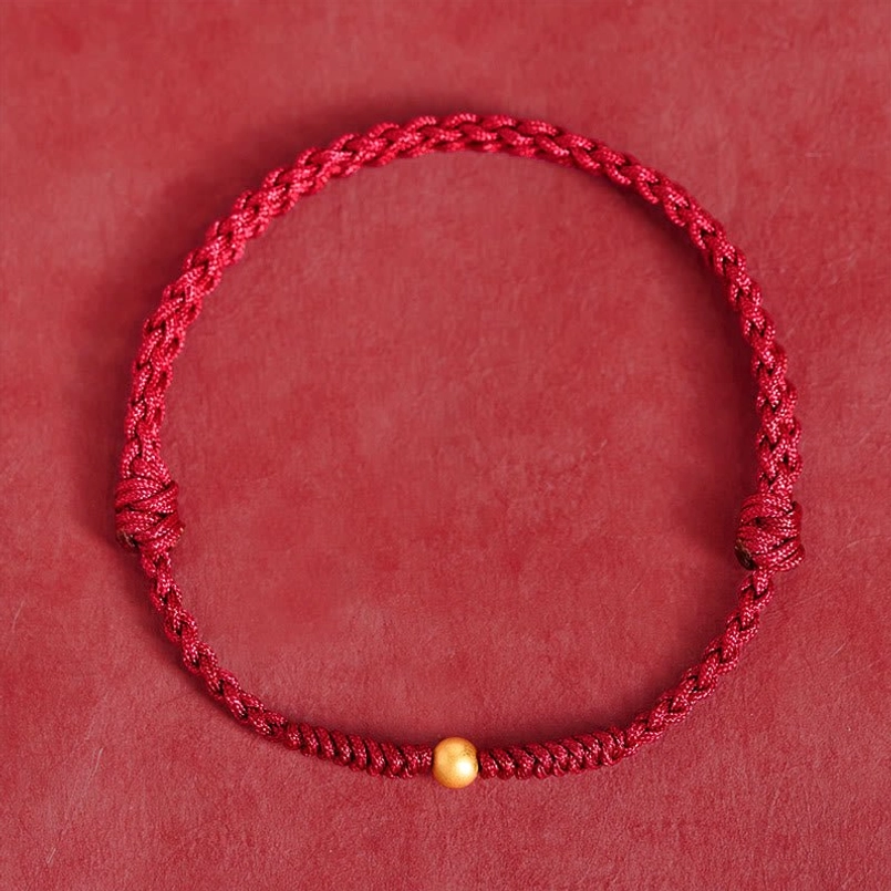 Red string bracelet with gold bead, flat lay top view on solid background