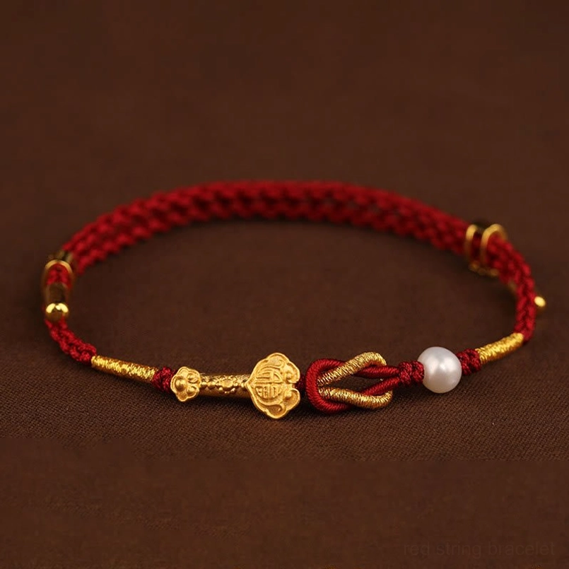 Red string bracelet with gold charms and white pearl viewed from above showing circular weave pattern