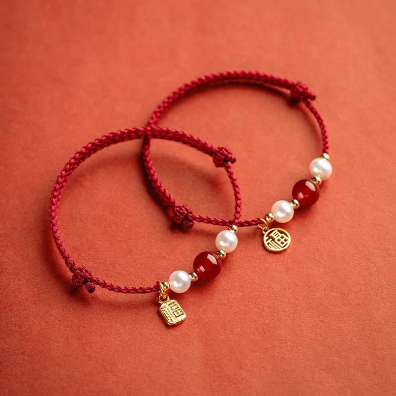 Two styles of adjustable red string bracelets with different gold pendants and pearl accents displayed side by side