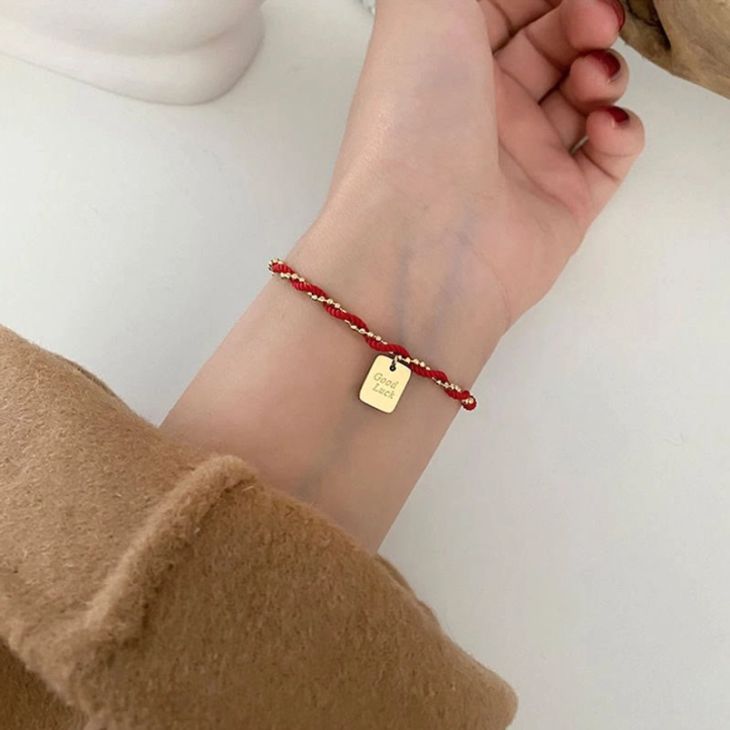 Red string gold charm bracelet minimalist product shot on white background