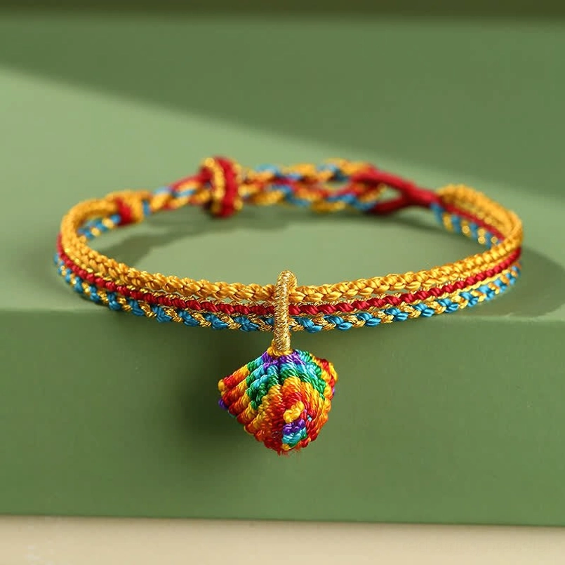 Colorful braided red string bracelet with decorative woven zongzi charm pendant on green background