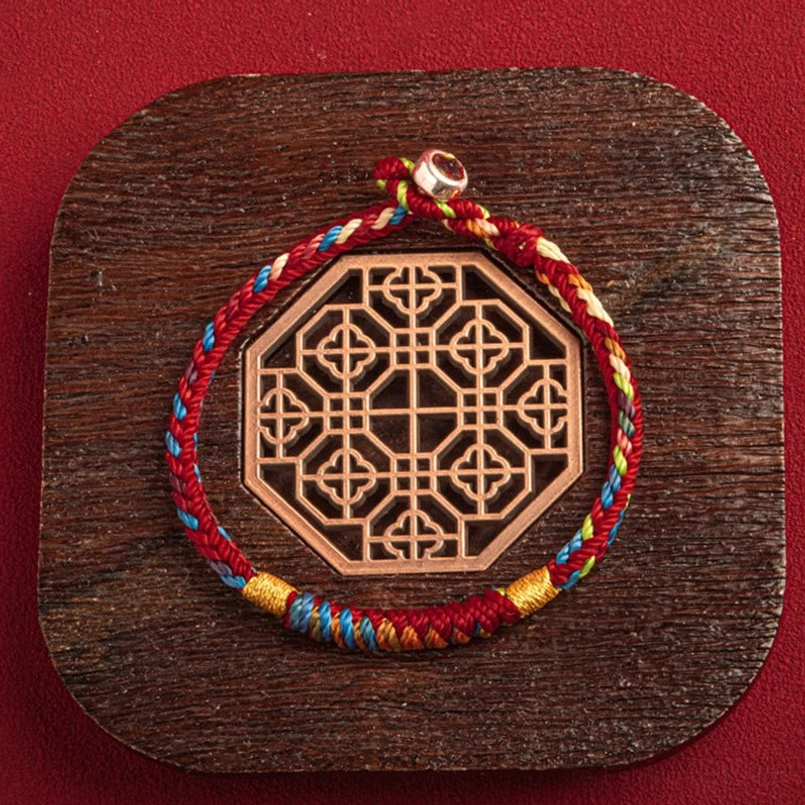 Red string bracelet with multicolor threads on traditional wooden coaster close-up