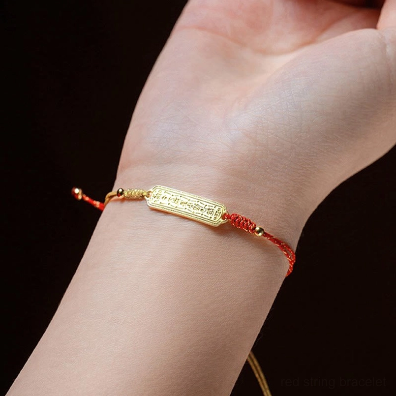 Red gold string amulet bracelet worn on left wrist close up view