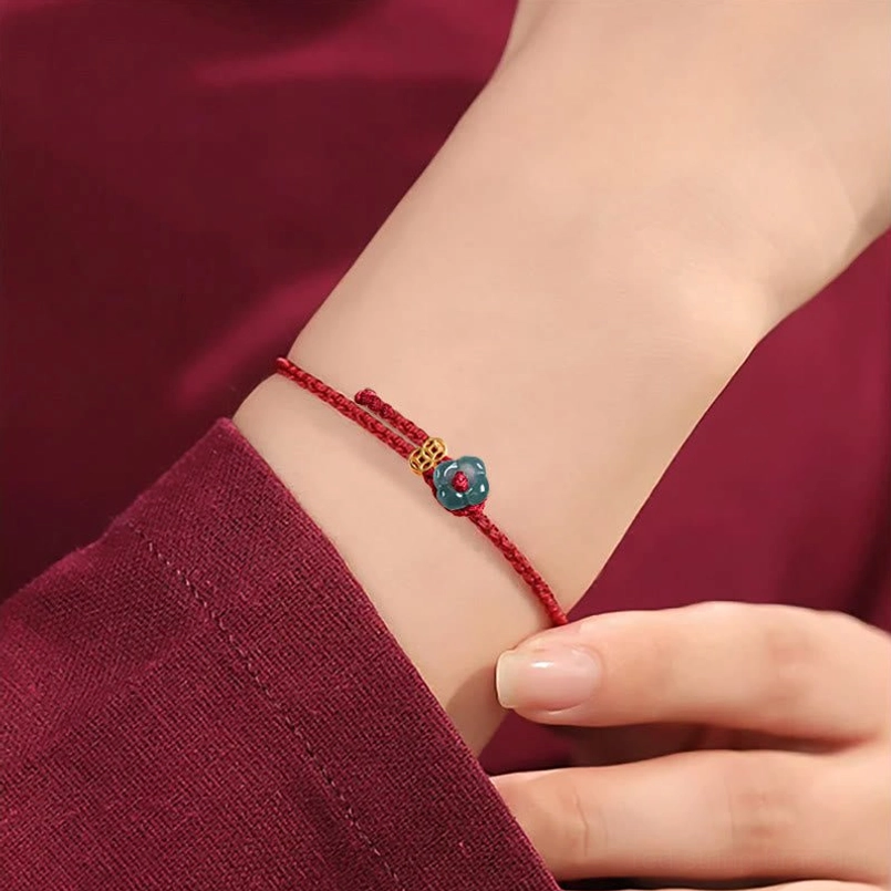 Red string bracelet worn on wrist with jade and copper coin charm close-up