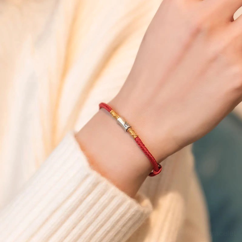 Red braided luck bracelet worn on left wrist with cream knit background