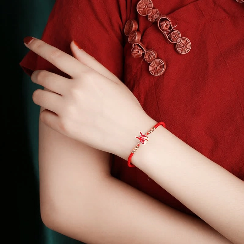 Red string bracelet with zodiac charm worn on wrist with traditional cheongsam background