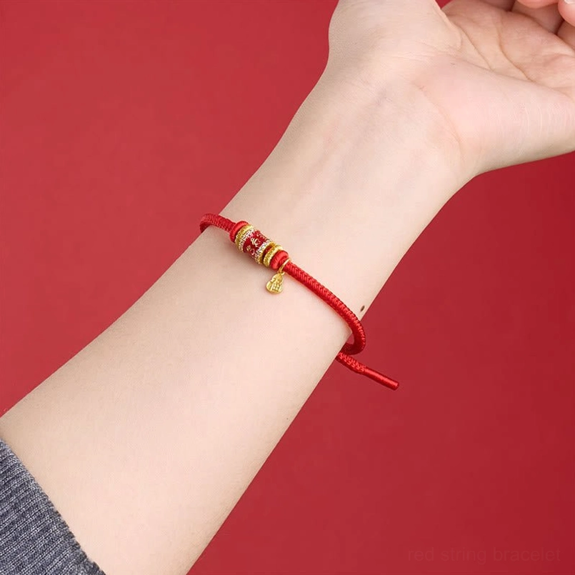 Worn red string protection bracelet on wrist showing slim cord and gold copper pendant details