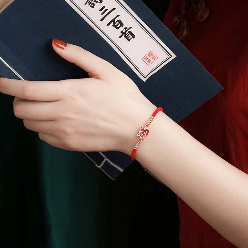 Lucky red string zodiac bracelet worn on wrist antique book background