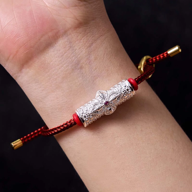 Red string bracelet with copper flower charm on wrist showing adjustable fit