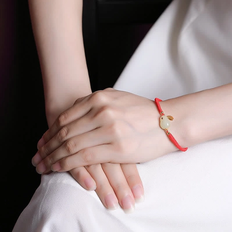 Adjustable red string bracelet with jade rabbit charm worn on female wrist for protection and luck