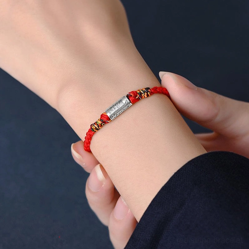 Red string bracelet worn on female wrist close-up with sterling silver colored knots