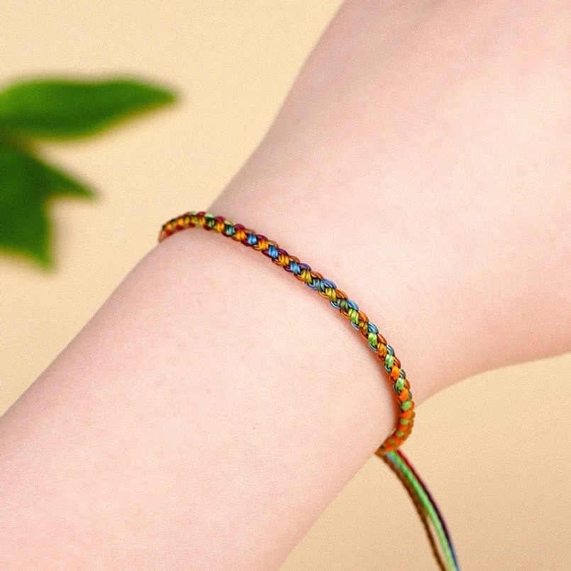Multicolored red string bracelet being worn on wrist showing slim braided design and fit
