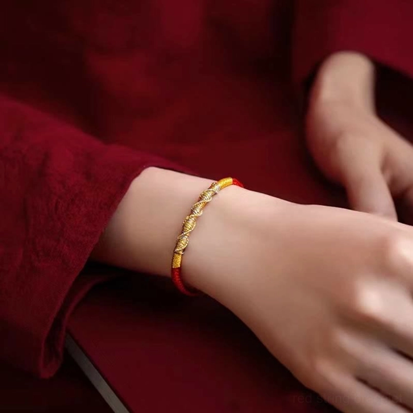 Red string protection bracelet with gold thread trim worn on wrist with red sleeve background