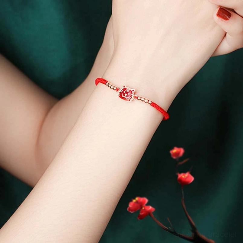 Red string lucky bracelet worn on wrist plum blossom dark green background