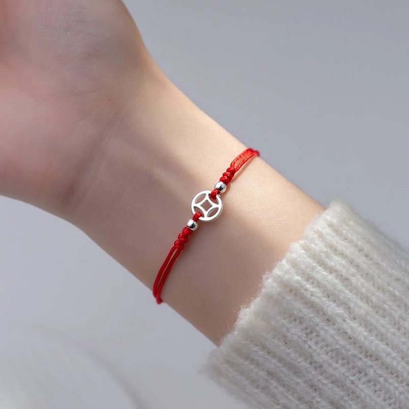 red string silver coin bracelet worn on wrist with white knitted sleeve indoor lighting
