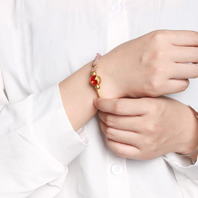 Red string bracelet on wrist with mountain-sea enamel charm, worn over white shirt background