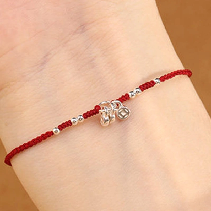 Red string bracelet with double silver copper coin charms worn on wrist showing handmade details