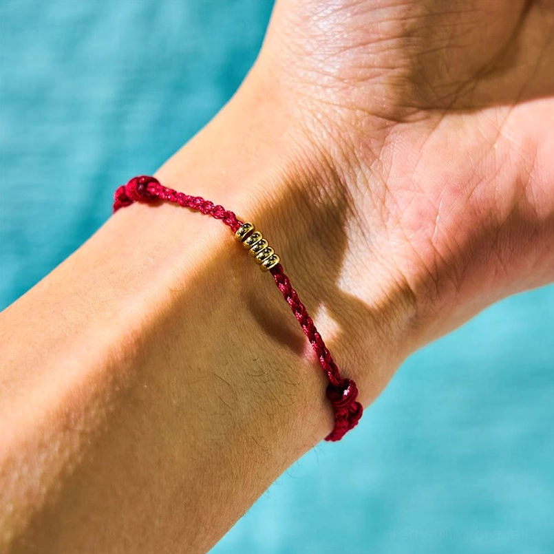 Red cord bracelet with golden metal beads worn on wrist close-up side view