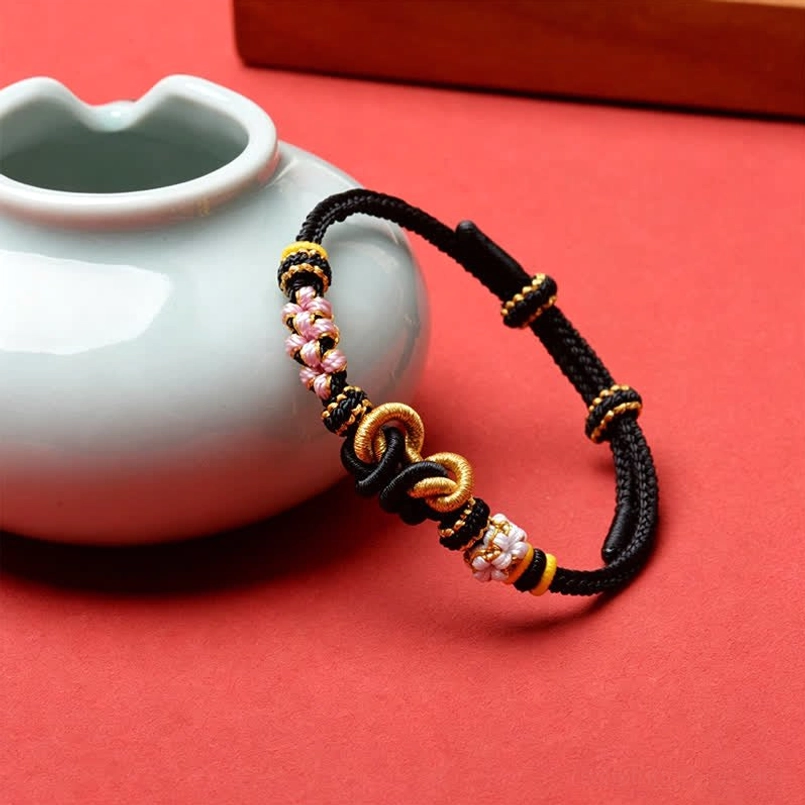 Two handmade red string butterfly protection bracelets displayed with ceramic tea ware side view