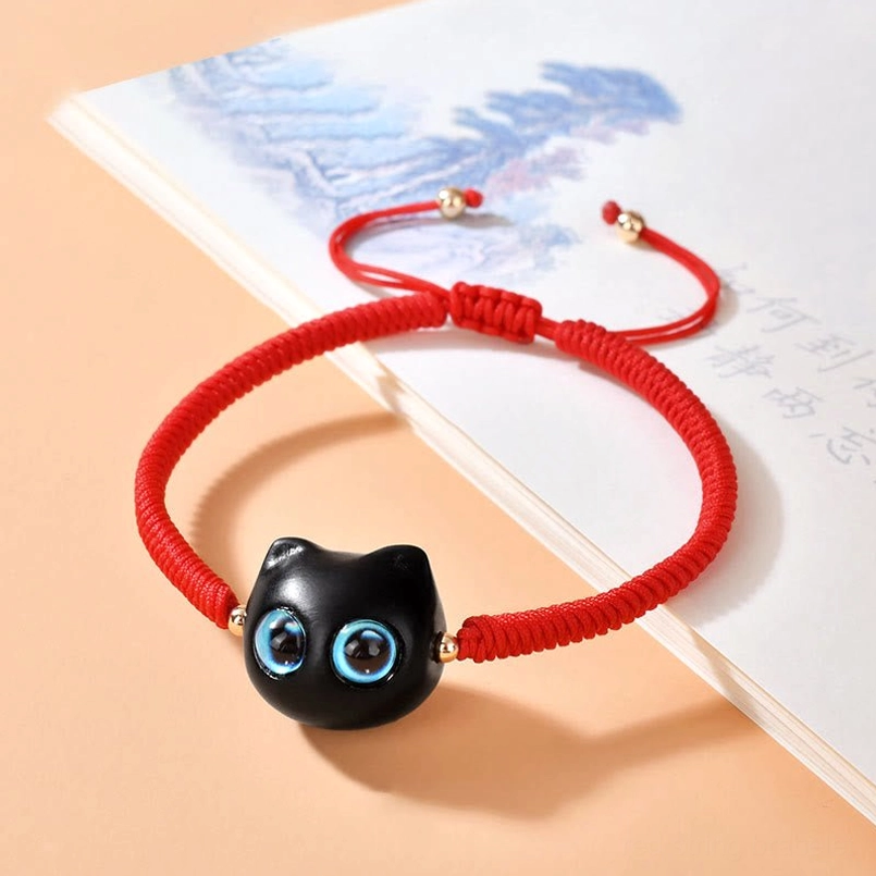 Bright red woven cat bracelet on Chinese book with detailed black cat charm