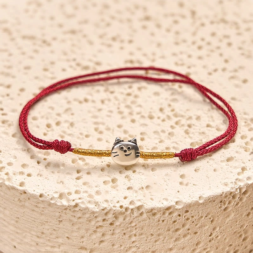 Close-up detail of double-layer red braided cord with silver cat charm and gold segments
