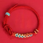 Red string Chinese knotting luck bracelet with floral woven trim and adjustable clasp, flat lay view