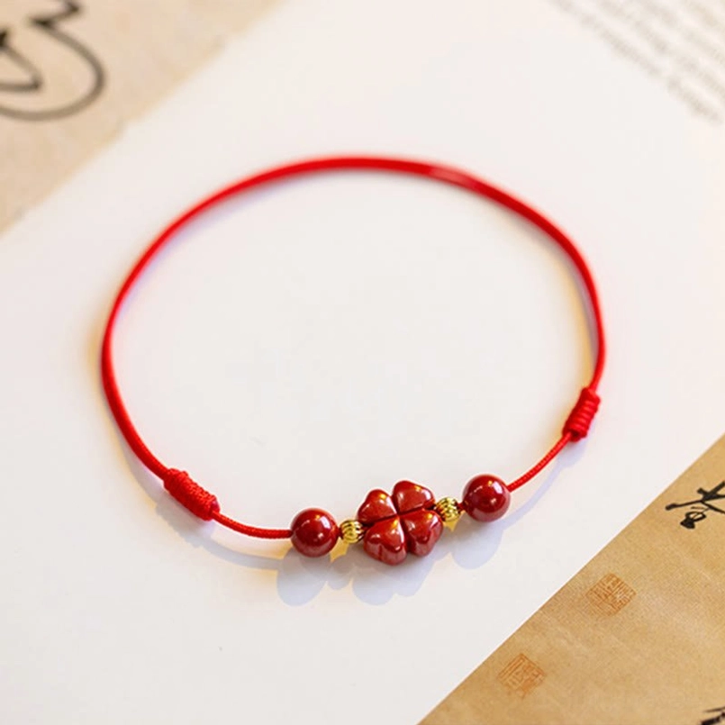 Side view close-up of red woven cinnabar string bracelet with knots and four-leaf clover on calligraphy paper