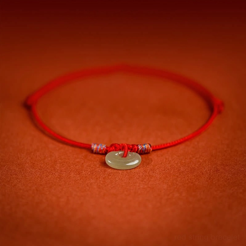 Red string pet collar with central jade donut pendant and colored knot accents, overhead view