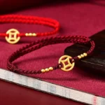 Red string copper coin braided bracelet with gold beads on velvet background
