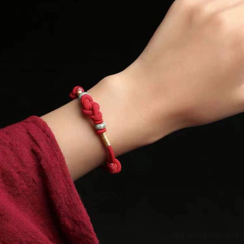 Slim red string couple bracelet worn on wrist with gold jade accents