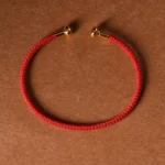 Red braided open cuff bracelet with gold metal end caps, top-down flat lay view on craft paper