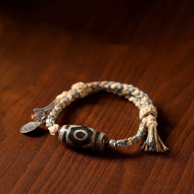 Top down view of Dzi Bead braided red string bracelet on dark brown wooden desktop