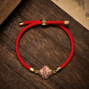 Red string four-leaf clover bracelet with Song brocade charm, flat lay view on dark wooden surface