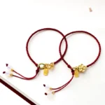 Two handmade red string Fu character lucky bracelets with peach blossom and bow knot gold charms displayed together