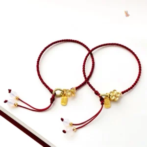 Two handmade red string Fu character lucky bracelets with peach blossom and bow knot gold charms displayed together