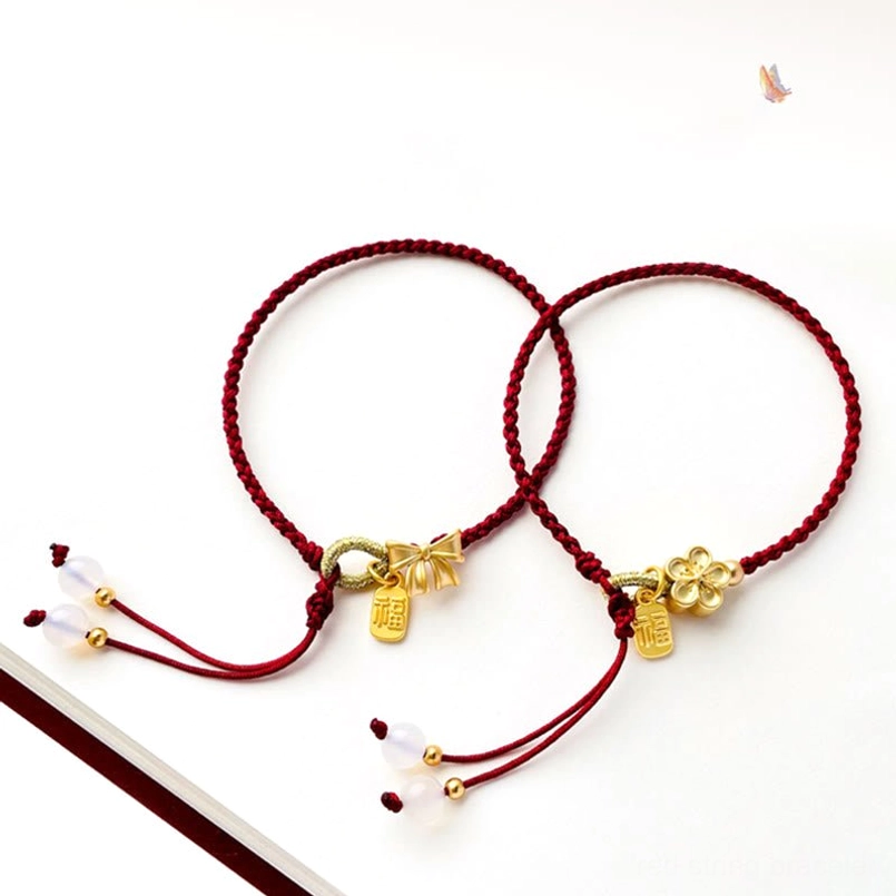 Two handmade red string Fu character lucky bracelets with peach blossom and bow knot gold charms displayed together