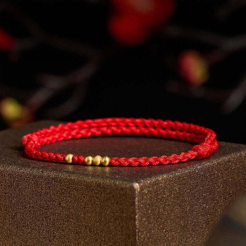 Red string gold bead bracelet low angle view on dark brown square platform