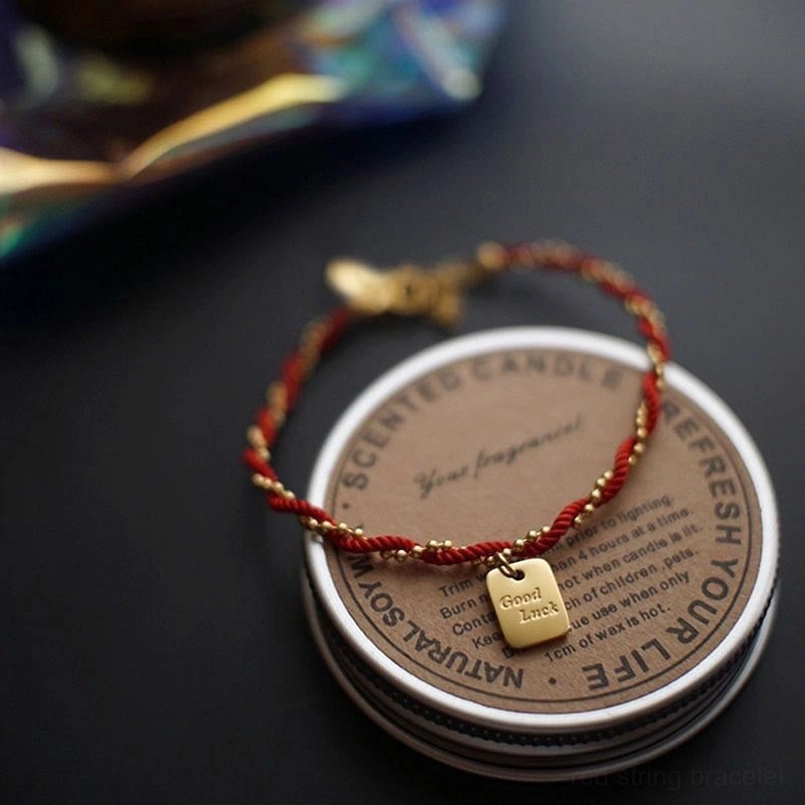 Red rope good luck bracelet placed on scented candle tin with metal buckle detail