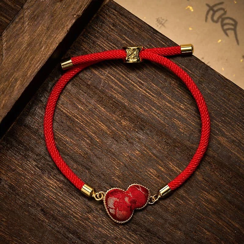 Handcrafted red string bracelet with gourd charm and adjustable sliding knot on dark wood surface