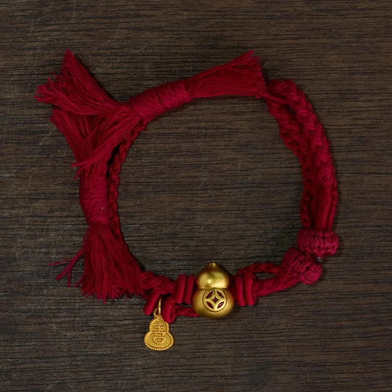 Thick red string bracelet with large gold gourd charm flat lay on dark wooden background