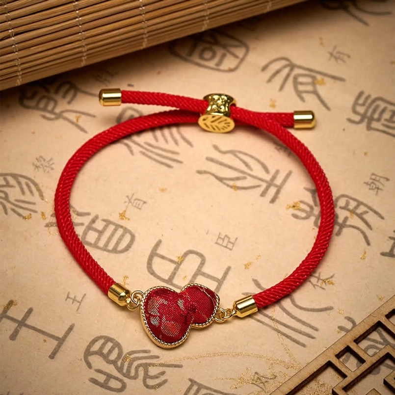 Red braided rope gourd protection bracelet with gold leaf engraved sliding lock on bamboo mat