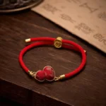Red string gourd protection bracelet with Song brocade charm on dark wooden desk with calligraphy paper