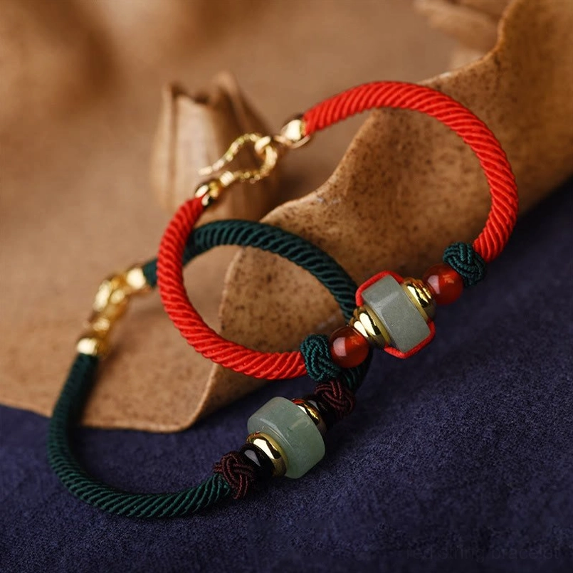 Two styles of handmade red string bracelets with green aventurine barrel beads and red agate accents, angled view