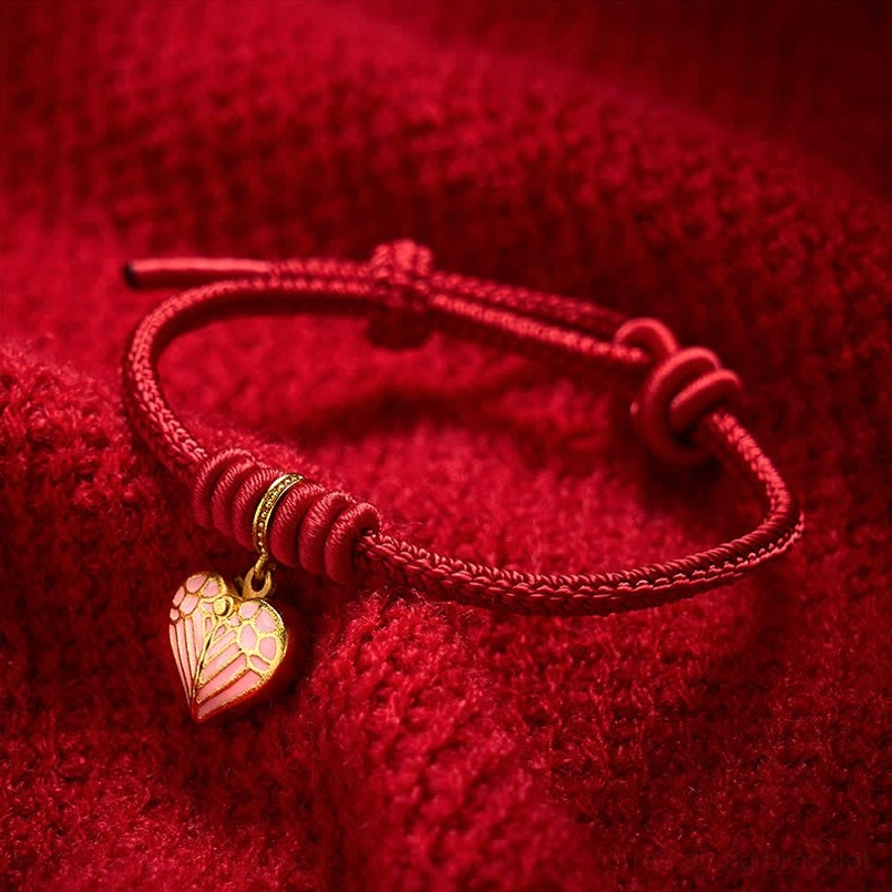 Close-up detail of braided red cord and small pink heart pendant with gold metal accent