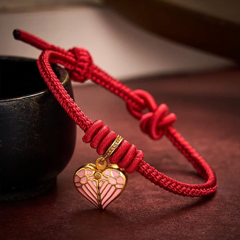 Red string bracelet with open-style pink enamel heart charm and gold hardware on dark table